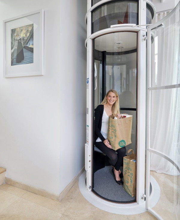 Woman sitting in a two-passenger elevator, carrying grocery bags.